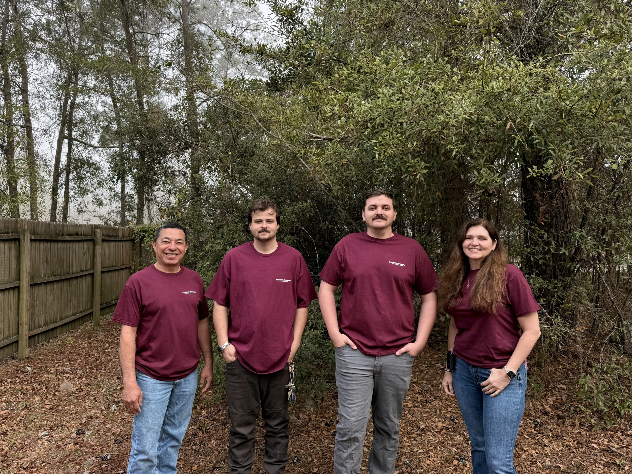 IMG_5690 Four members of the Phoenix Builders team standing together in front of a wooded area and a wooden fence